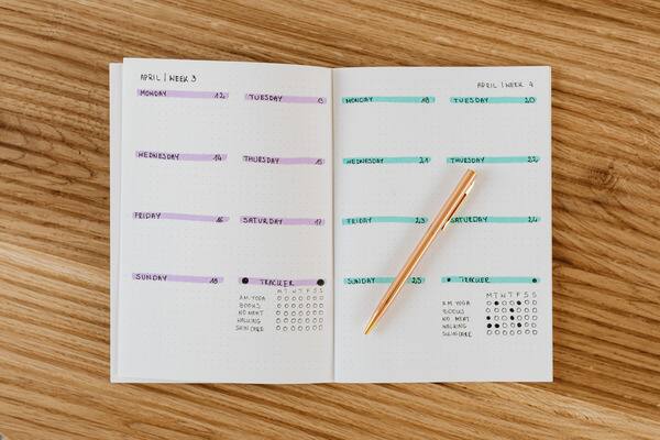 Open weekly planner with a gold pen on a wooden desk, showing days of the week and dates for April 2023.