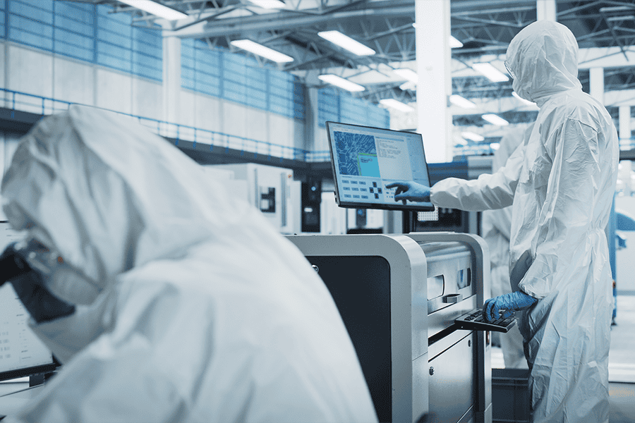 Cleanroom staff operating manufacturing equipment and reviewing process data on monitors in a controlled facility.
