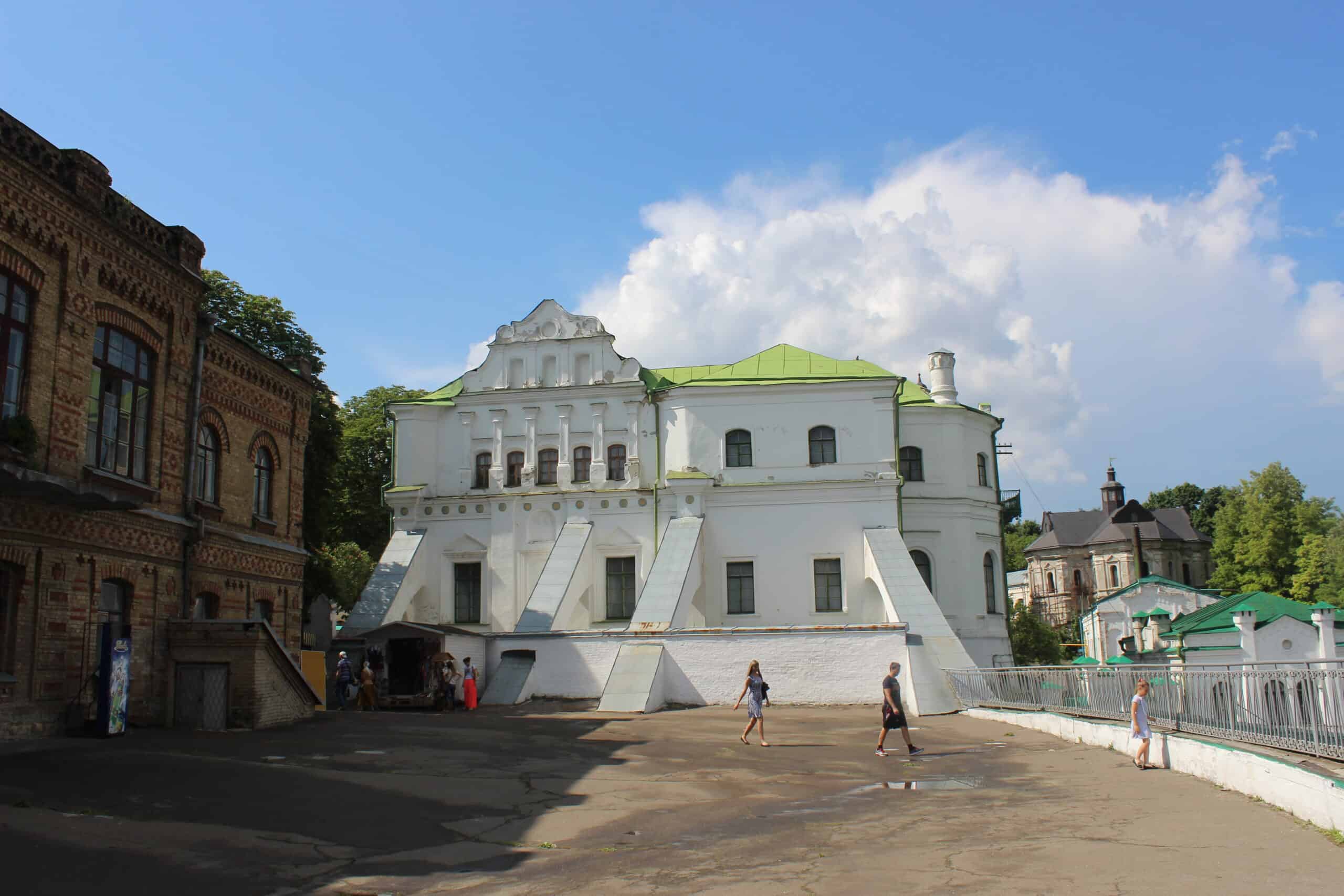 Історична будівля з білою фасадою та зеленим дахом на фоні неба з хмарами.