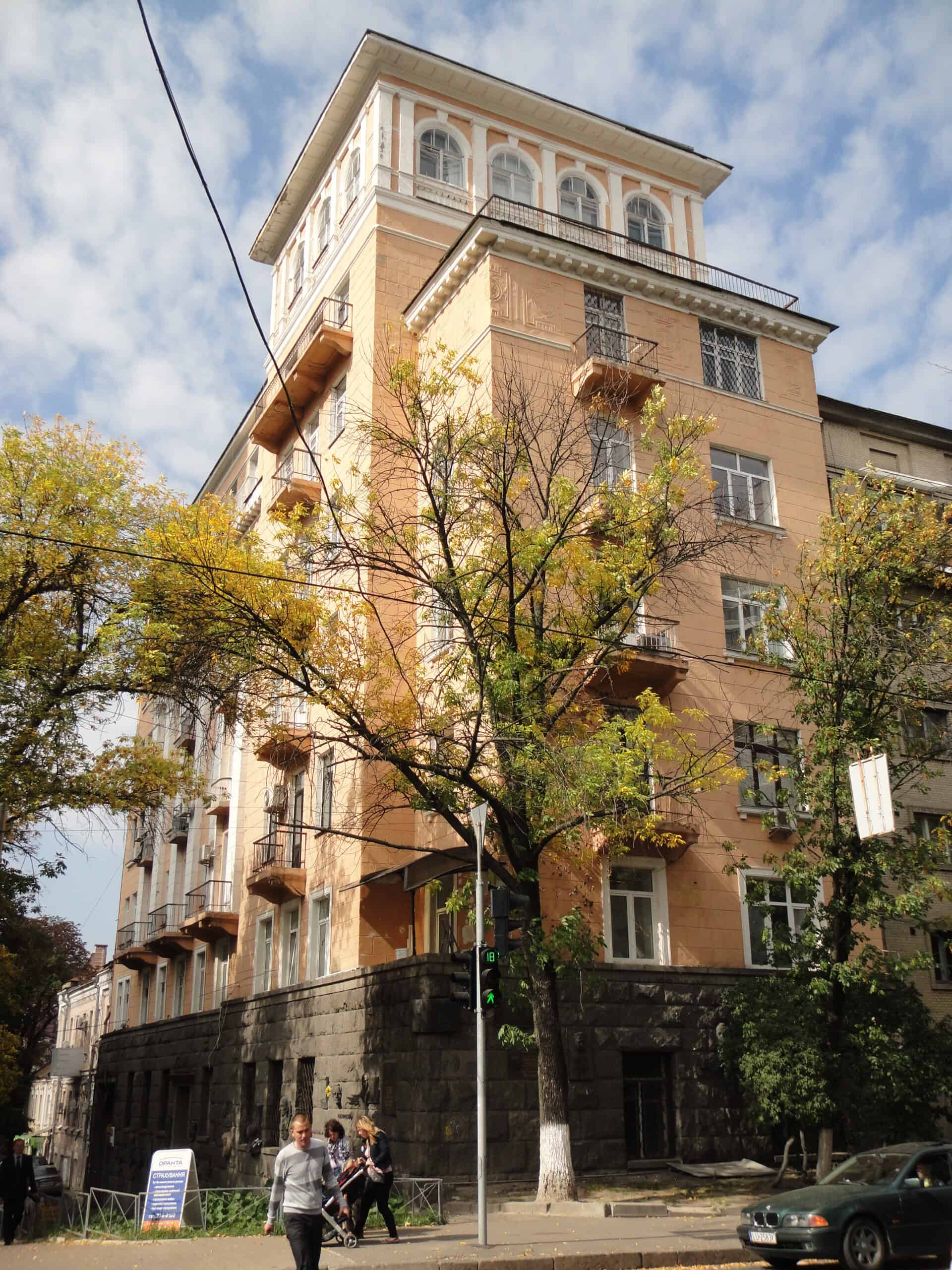 Історична будівля з балконами та деревами на вулиці, архітектура початку ХХ століття.