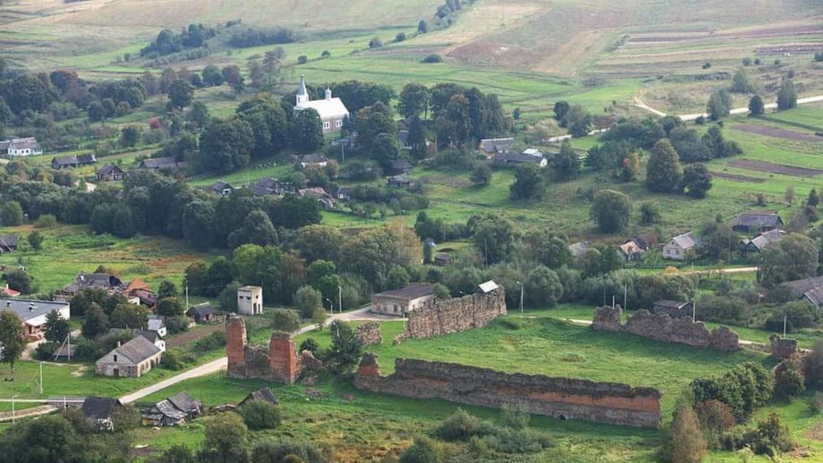 Історична панорама села з руїнами та зеленими полями.