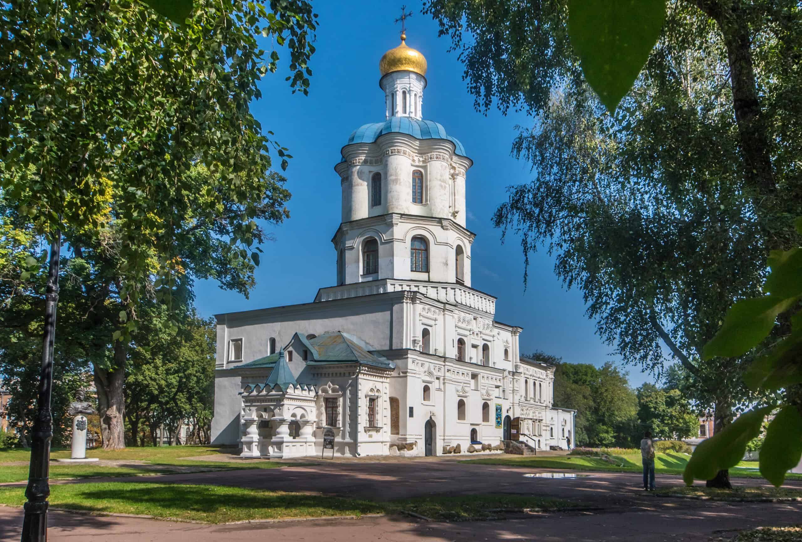 Барокова церква з золотим куполом на фоні зелених дерев і ясного неба.
