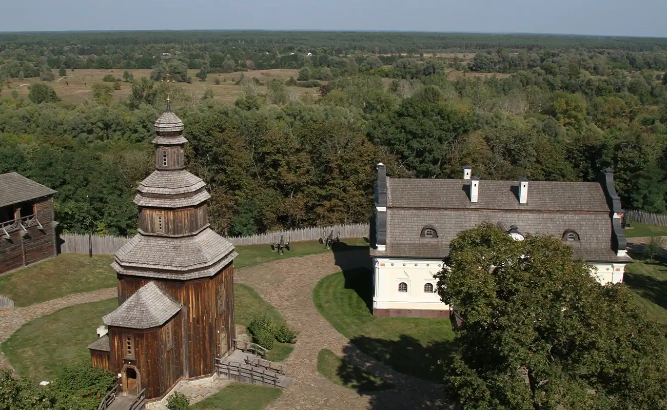 Історичний дерев'яний храм і церква на фоні зелених лісів і полів у Україні.