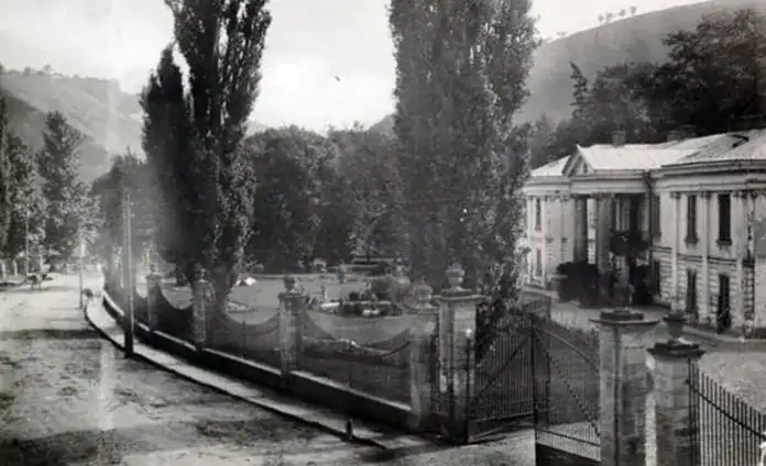 Історична фотографія парку з старими будівлями та деревами у чорнобілому стилі.