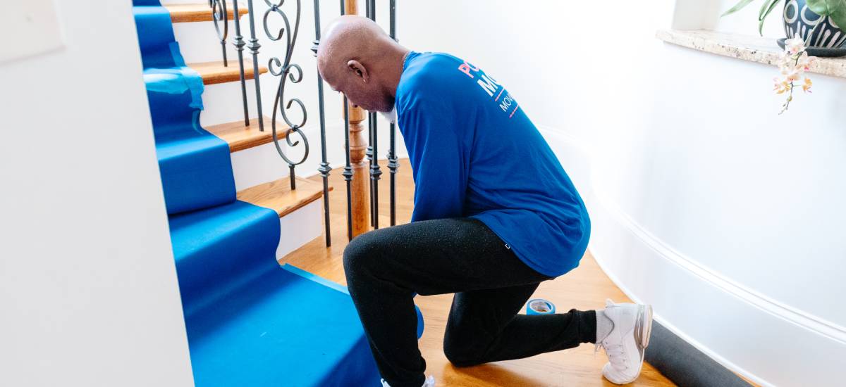 Port City Movers staff securing blue protective covering on wooden stairs during a moving project.