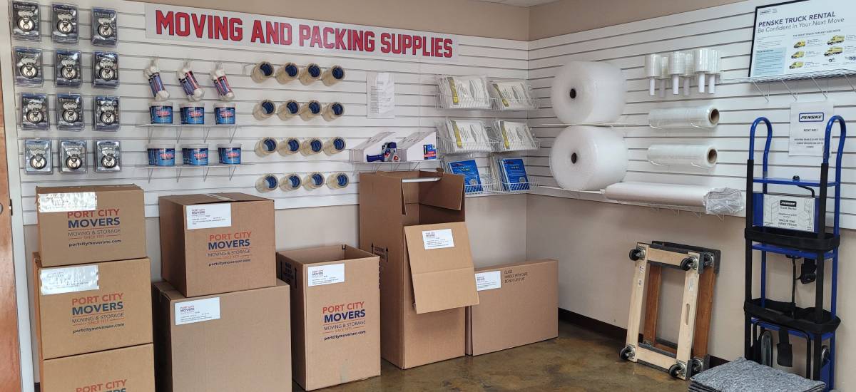 Display of moving and packing supplies including boxes, tape, bubble wrap, and dollies at Port City Movers store.