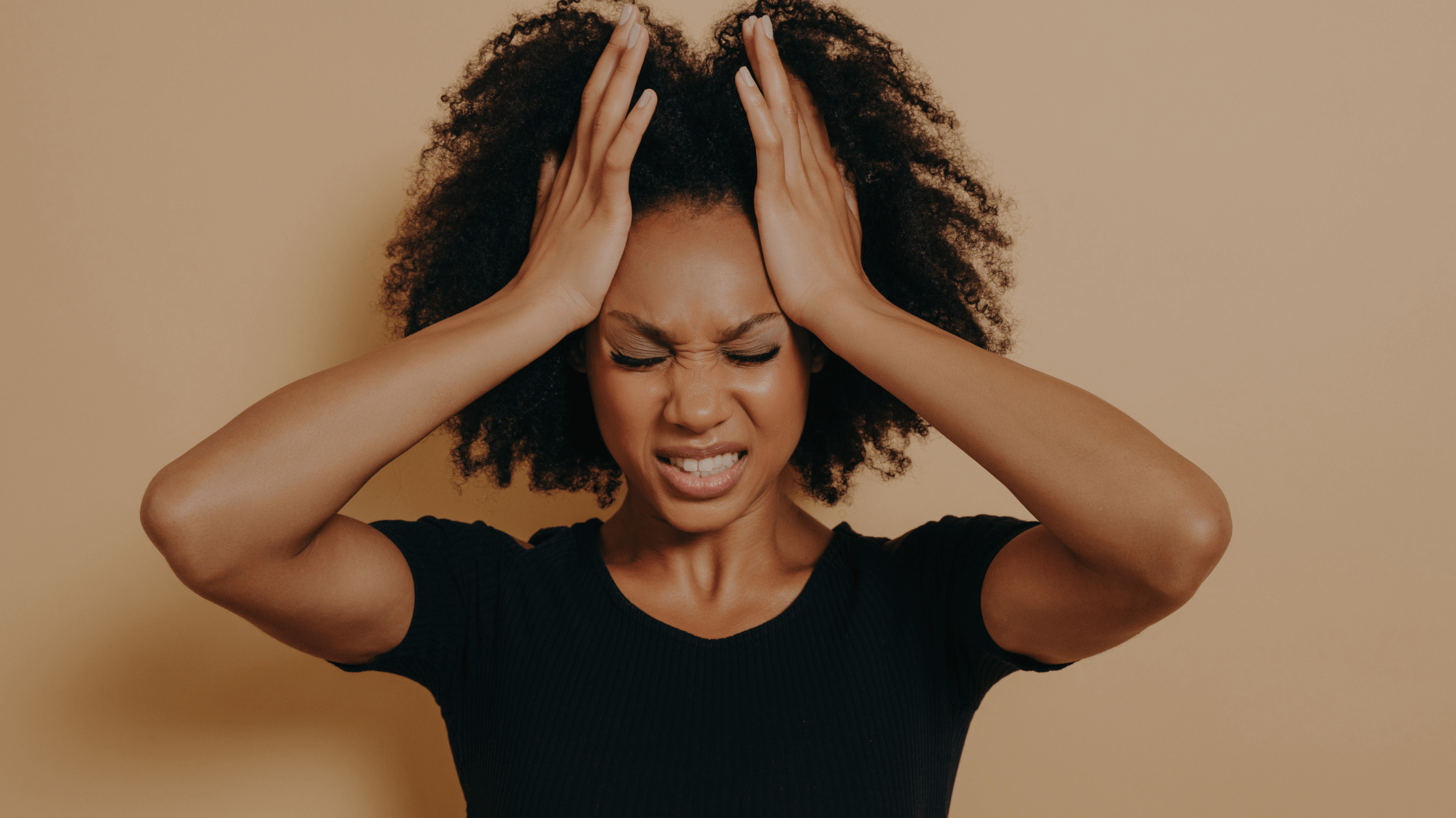 A woman with her hands on her head, eyes closed and teeth clenched, illustrating the physical and emotional distress of chronic pain and stress.