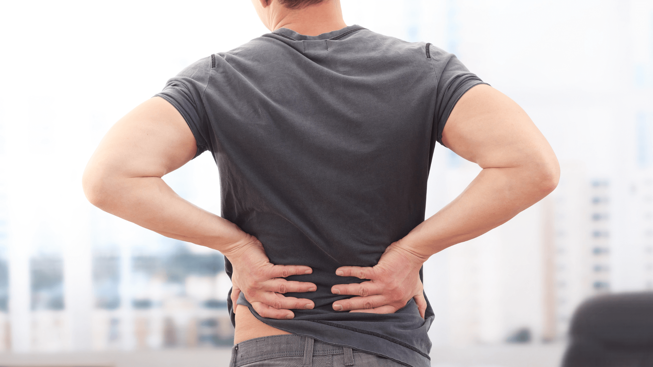 A man stands with his back to the camera, clutching his lower back with both hands, visually representing the common pain and discomfort experienced by patients with sciatica or sacroiliac (SI) joint pain.