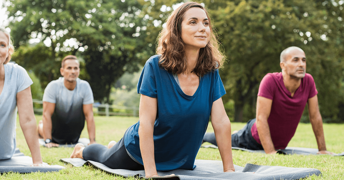 A group of adults practices gentle yoga outdoors on mats, performing a cobra pose with a calm expression, symbolizing physical therapy and gentle movement for pain management and improved flexibility.