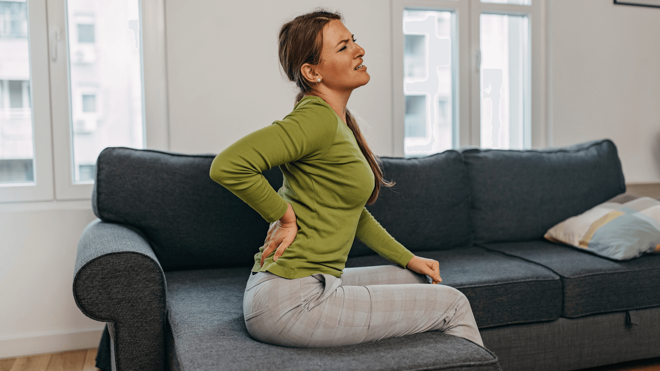 A patient sitting on the edge of a bed holding their lower back in frustration, illustrating chronic pain that persists after previous treatments.