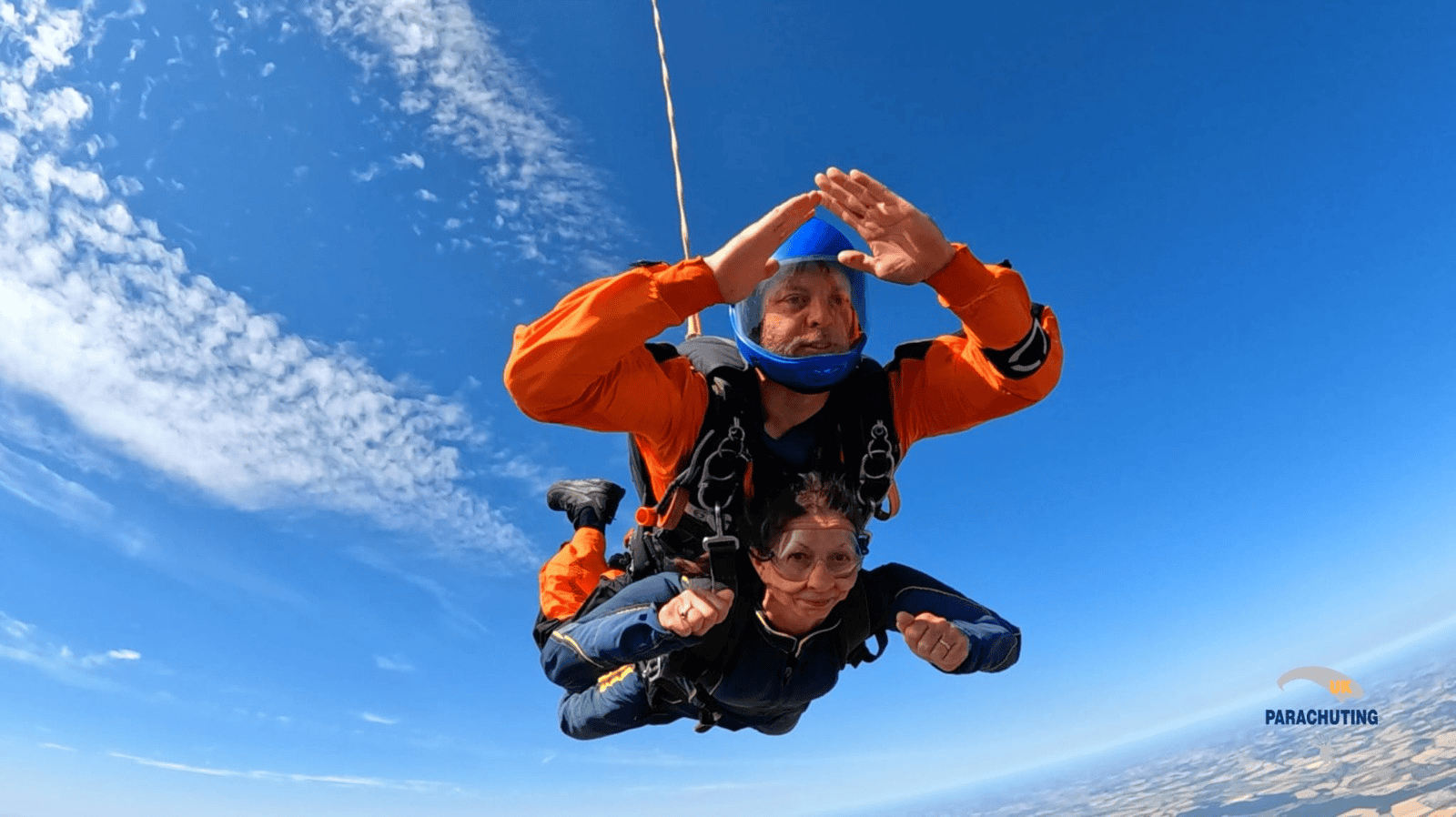 A Love Story Takes Flight: Couple Celebrate 40 Years With One Final Skydive | Private Gp Clinic | West Byfleet | Sunningdale | Reigate | Farnham | Wokingham | Putneymead Couple Skydiving In Clear Blue Sky With Parachute Gear.
