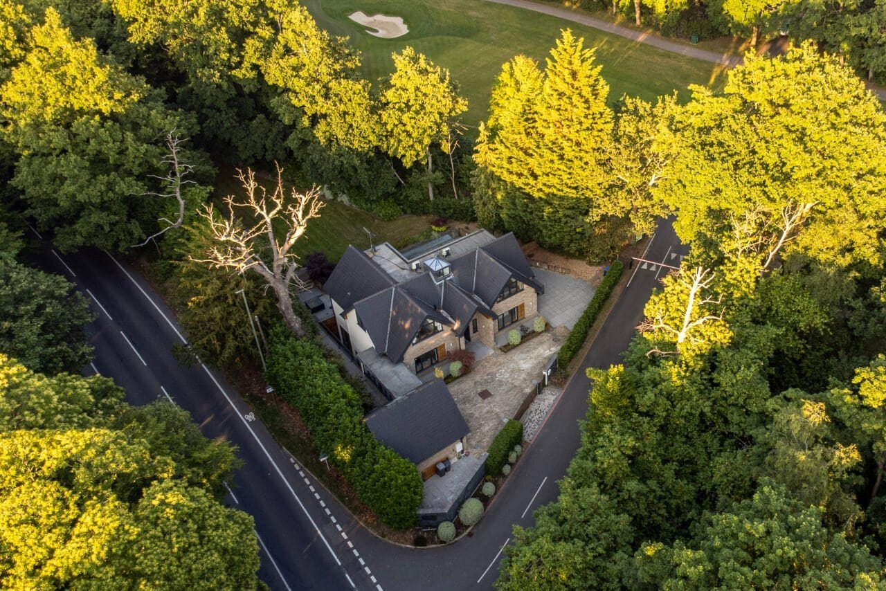 Aerial view of a detached house surrounded by lush green trees and garden in the countryside.
