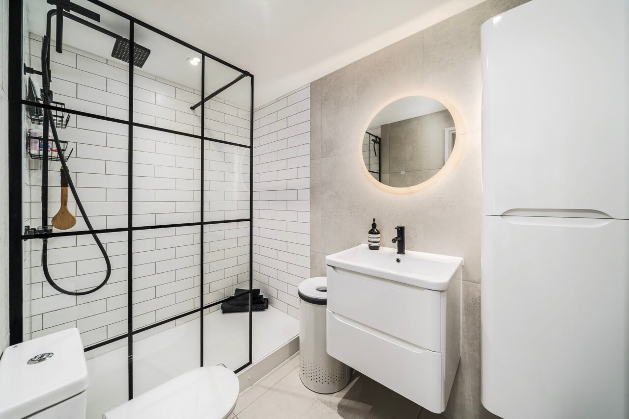 A modern bathroom with walk-in shower, white tiles, and minimalist vanity unit.