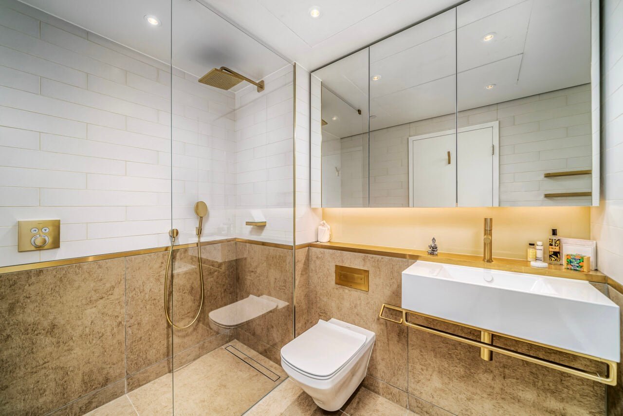 A modern bathroom with white tiles, gold fixtures, and a walk-in shower.