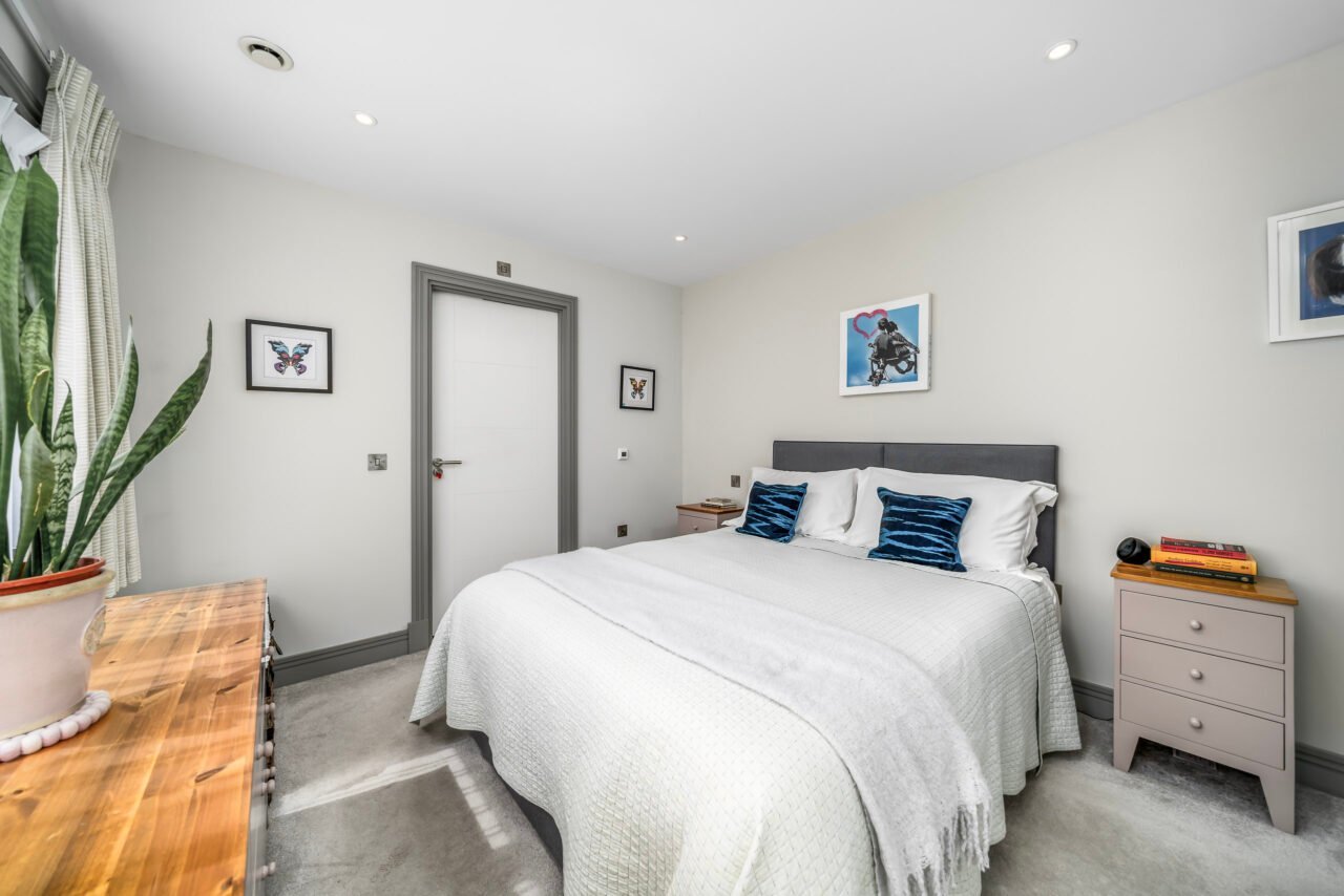 A modern, well-lit bedroom with white walls, grey furniture, and colourful artwork.