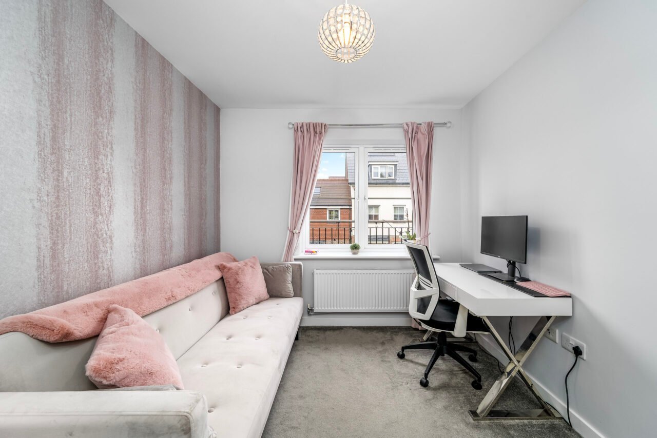 A comfortable home office with a white desk, black chair, and pink curtains.