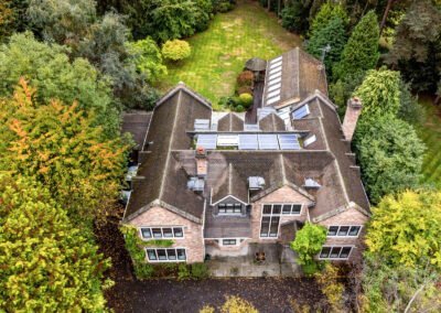 Aerial view of a large detached house surrounded by lush greenery and mature trees in a garden setti.