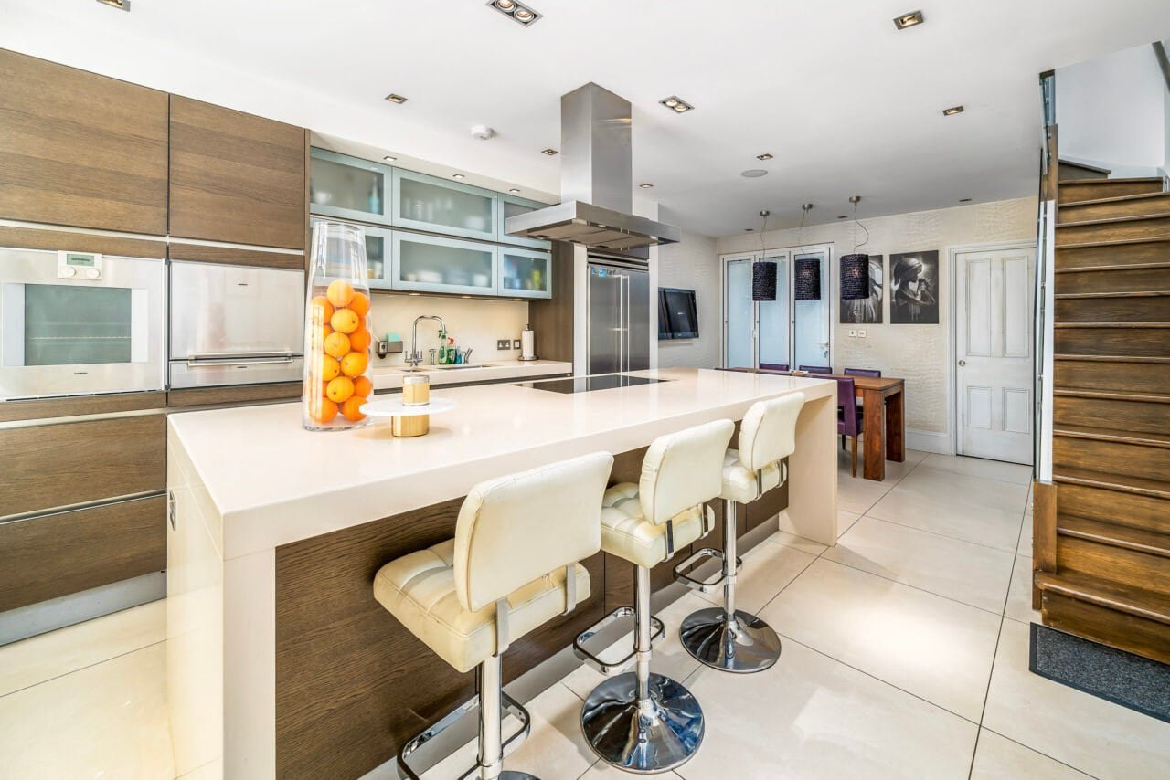 A modern kitchen with white island, wooden cabinets, and bar stools, bright and spacious.