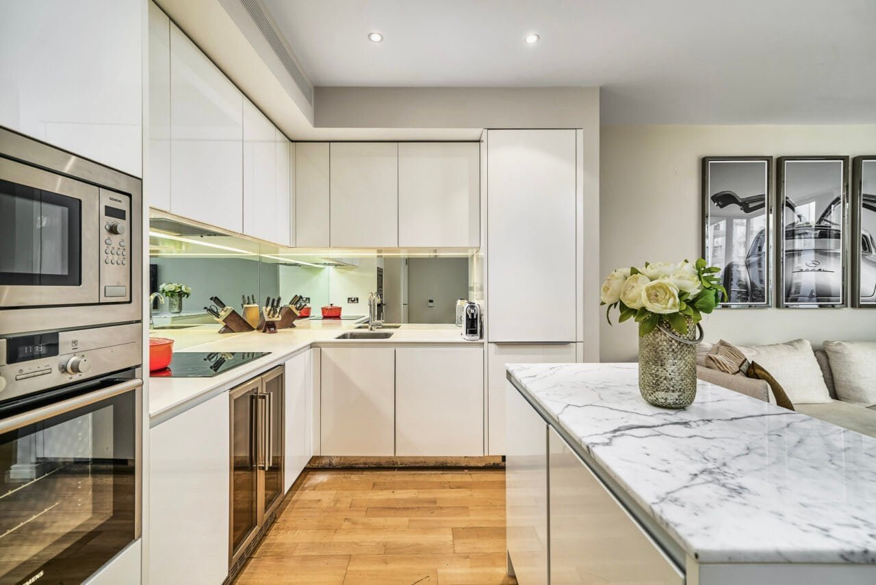 Modern white kitchen with marble island and wooden flooring, bright and stylish interior.