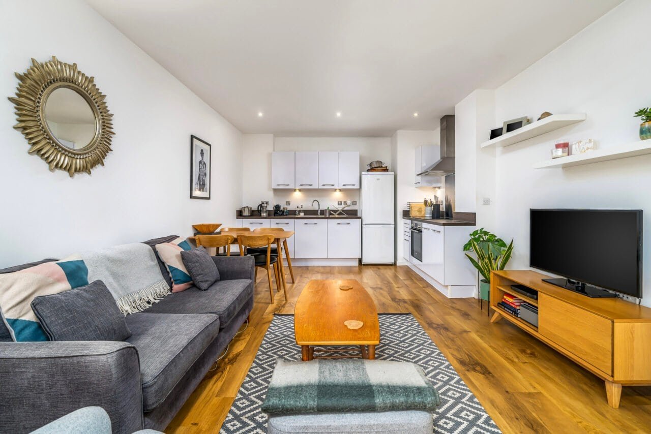 Modern open-plan living room with kitchen, wooden flooring, and TV area.