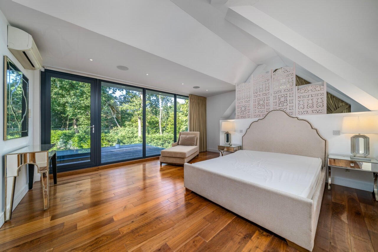 A spacious modern bedroom with large glass doors overlooking greenery and wooden flooring.