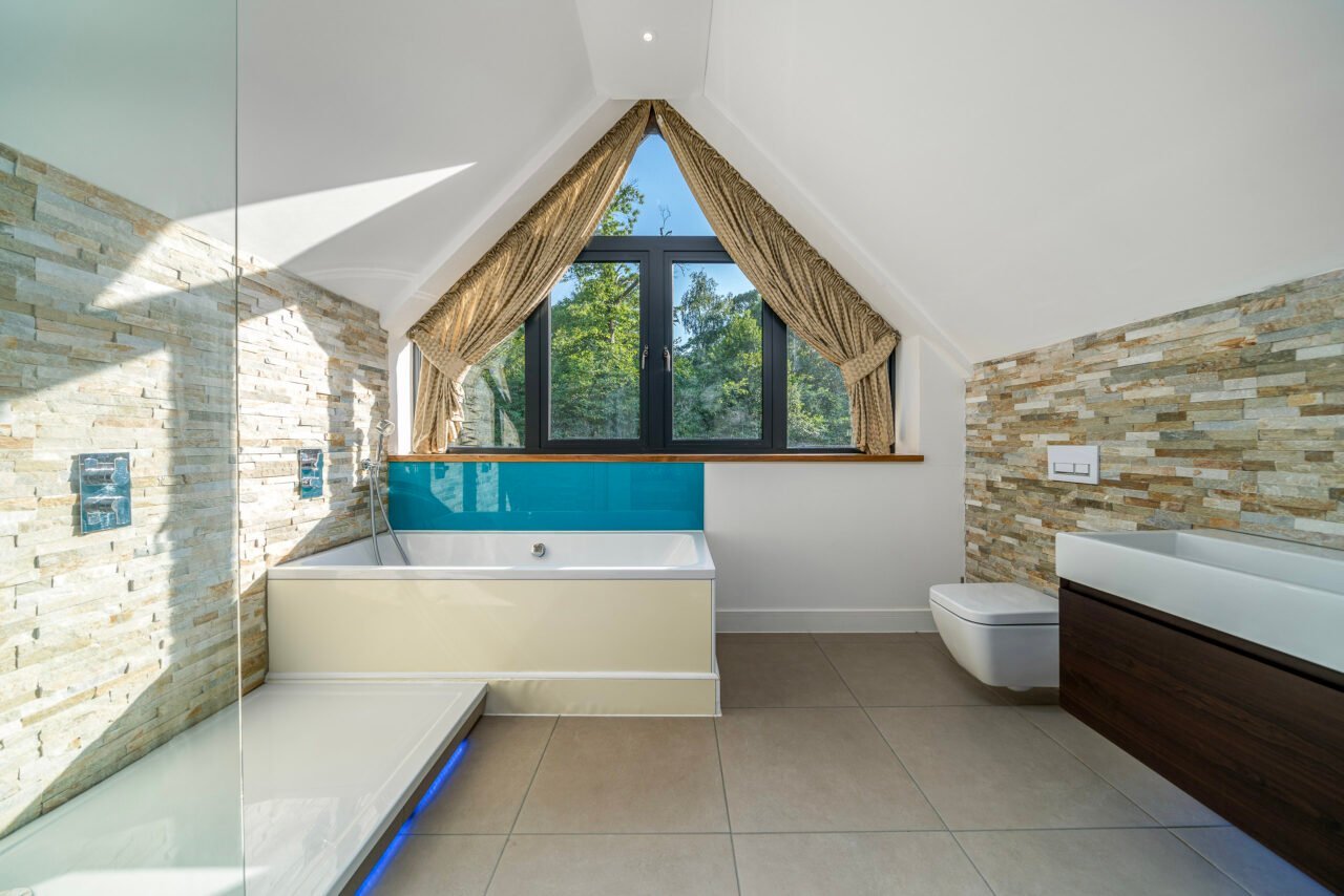 Modern bathroom with bathtub, stone wall accents, and large window with curtains.