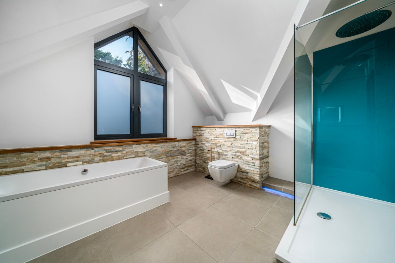 A modern bathroom with a sloped ceiling, large window, and walk-in shower.