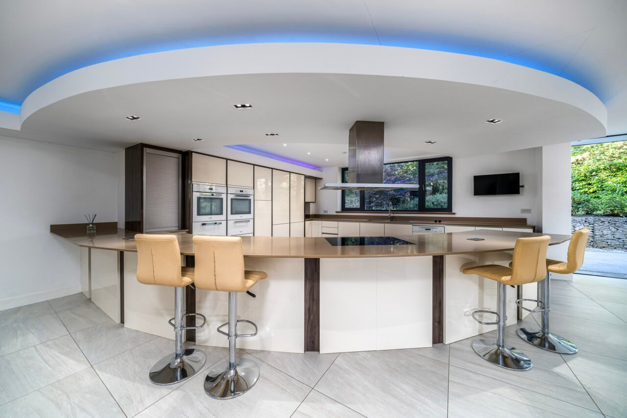 Modern kitchen with curved island, beige bar stools, and built-in appliances.