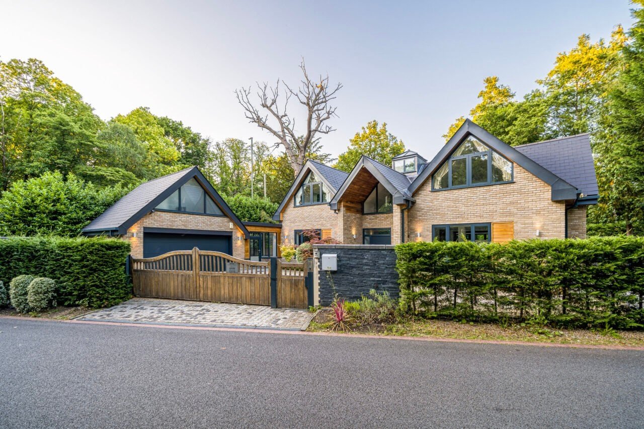 A lush modern detached house with a gated driveway and surrounding greenery.