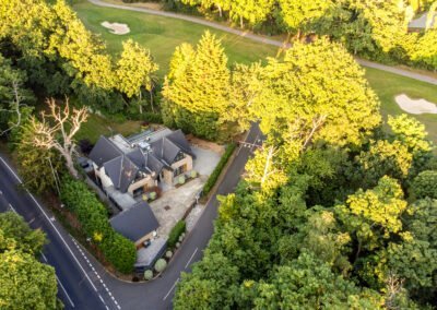 Aerial view of a modern house surrounded by lush green trees and a golf course in the background.