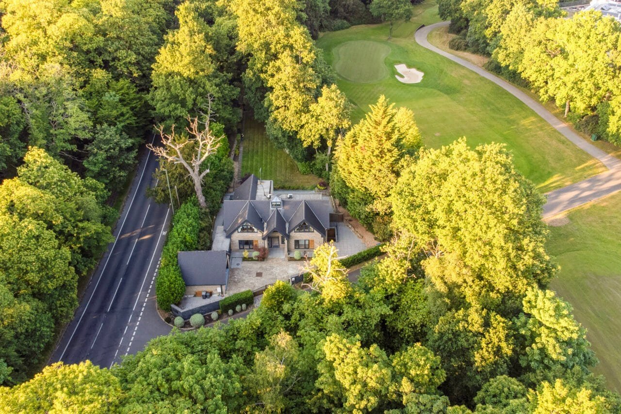 Aerial view of a house surrounded by lush green trees and a golf course in the background.