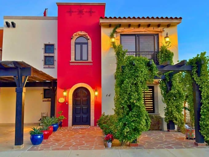 Colorful Mediterranean-Style Villa At Quivira Los Cabos With Vibrant Exterior, Lush Greenery, And Charming Architectural Details, Showcasing Luxurious Living In A Premier Real Estate Development.