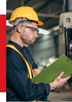 Industrial automation technician inspecting equipment with tablet in manufacturing facility.
