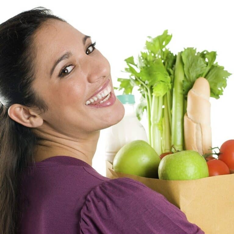 Woman holding a bag of fresh organic vegetables including lettuce, apples, and tomatoes.