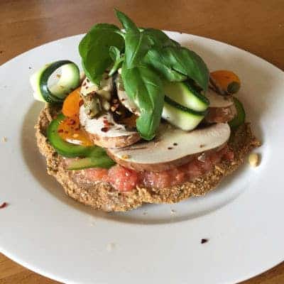 Fresh Mediterranean open faced sandwich with vegetables and herbs on a white plate.