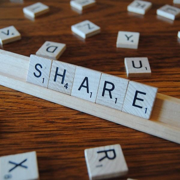 Wooden surface with Scrabble tiles spelling "SHARE" and scattered letter tiles.