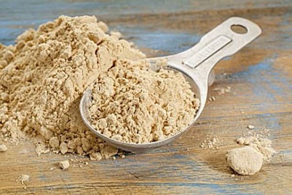 Organic protein powder in a metal scoop on a wooden surface, healthy supplement.