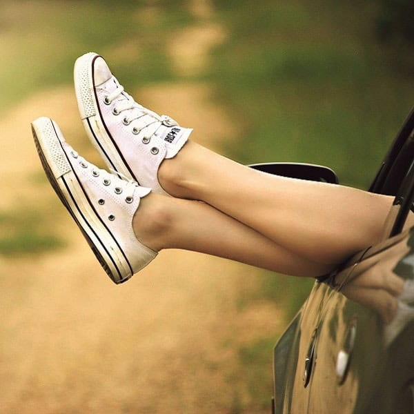 White Converse sneakers with legs hanging out of a car window, enjoying a relaxed outdoor moment.