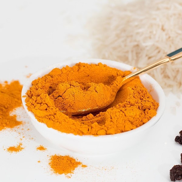 Golden turmeric powder in a white bowl with a spoon, on a white surface.