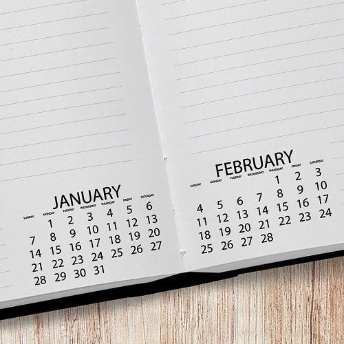 February calendar pages open, showing dates and days, on a wooden surface.