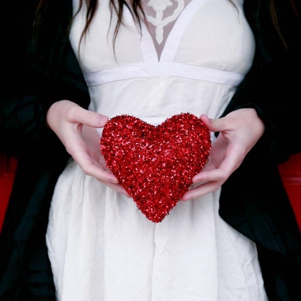 Shaped red glitter ornament held by woman in white dress, symbolizing love and affection.