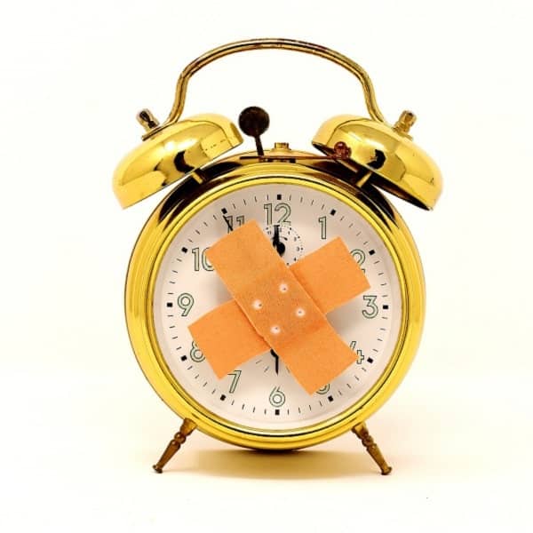 Vintage gold alarm clock with bandages on the face, symbolizing time and healing. Perfect for themes related to health, wellness, and time management.