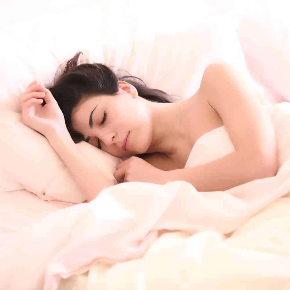 Sleepy woman resting peacefully in bed, promoting better sleep habits to beat ‘coronasomnia’.