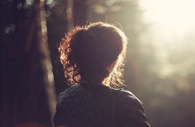 Woman with curly hair in a forest during sunset, peaceful and reflective scene.