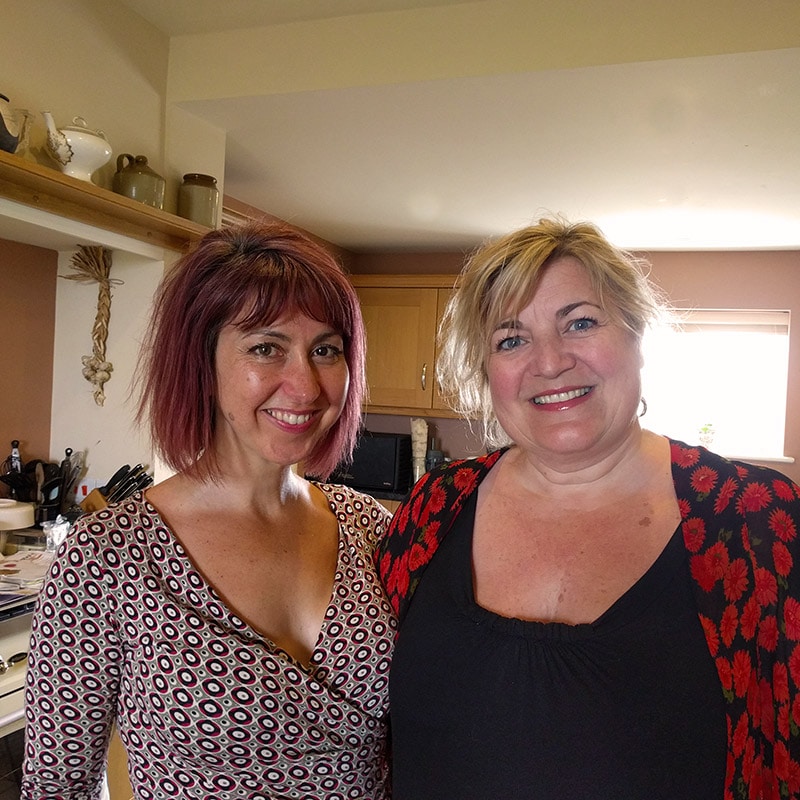 Women smiling in a cozy kitchen, enjoying a friendly moment together.