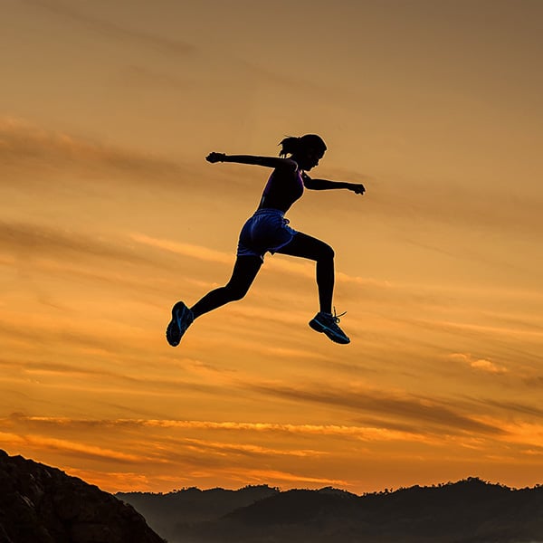 Girl jumping in the air during sunset with scenic mountain background.