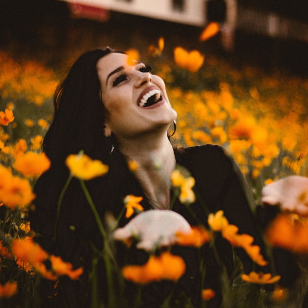 Happy woman surrounded by vibrant orange flowers, expressing joy and freedom outdoors.