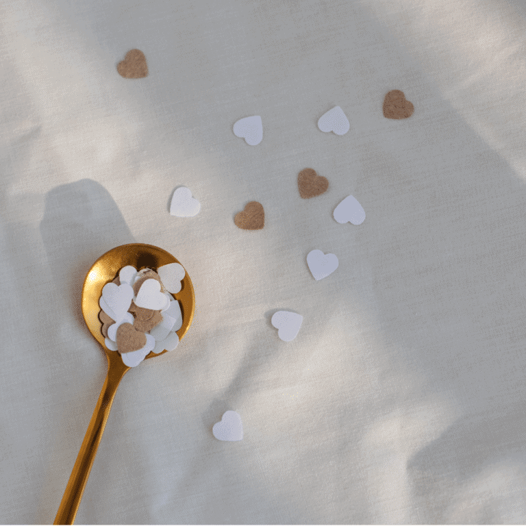 Heart-shaped confetti scattered on white surface with a gold spoon.