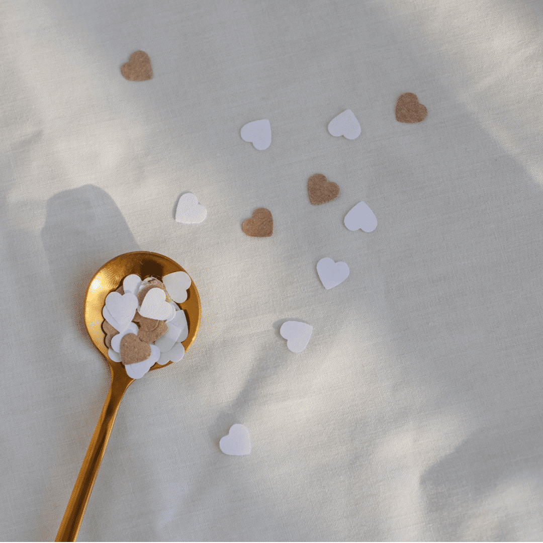 Heart-shaped confetti scattered on white surface with a gold spoon.
