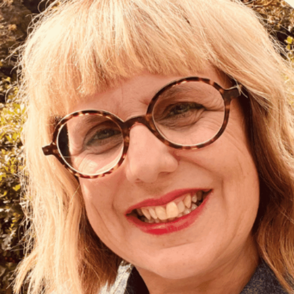 Woman with blonde hair and glasses smiling outdoors, natural sunlight.